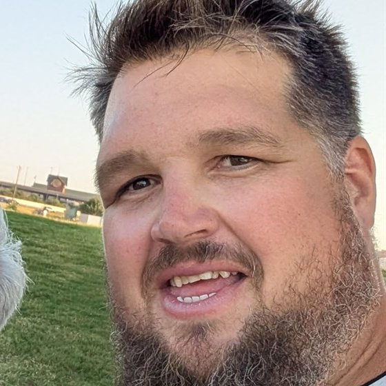 Dusty Stilwell outdoors at golden hour, mid-sentence, smiling, with a beard and spiked hair.